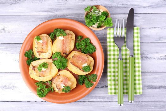 Baked potato with bacon on plate, on wooden background