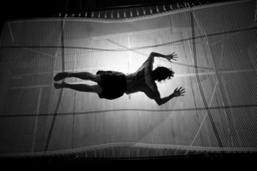 silhouetted man landing with stomach on trampoline