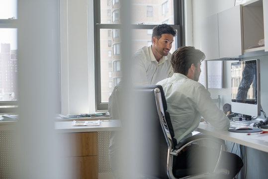 Two men by a computer screen, talking and planning. 