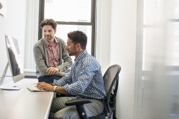 Two business colleagues in an office talking and referring to a computer screen. 