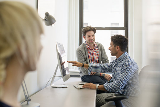 Three business colleagues in an office, two talking and one standing by the door. 
