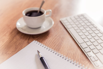 Office table with notepad, computer keyboard and coffee cup  and