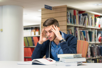 Bored male university student in the library studying for exam