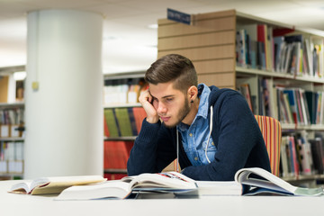 Bored male university student in the library reading books