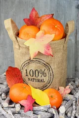 Tapeten Jute zak met mandarijnen en herfstbladeren © trinetuzun