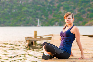 Fototapeta na wymiar young brunette sitting on a pier in the lotus position