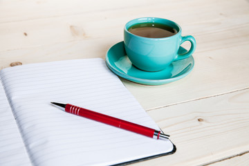 Open a blank white notebook, pen and cup of tea on the desk