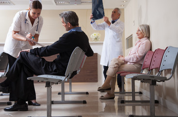 Doctors reviewing x-ray at hospital reception while people sitti