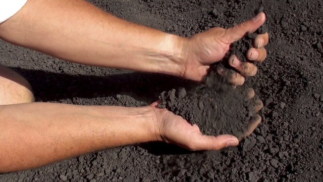 Hands strew a slag lava sand from the mount Etna.