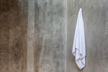 The white towel is hanging on a hanger with concrete wall in the