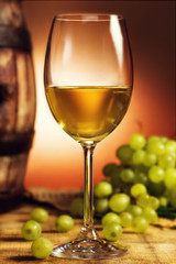 Glass of white wine in front of green grapes and old barrel