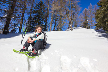 Ragazza seduta su neve con ciaspole