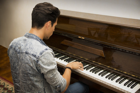 Young handsome male artist playing classical upright piano