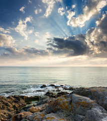 beautiful seascape at sunrise. sunbeams on the cloudy sky. waves crashing on coast with boulders