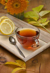 glass cup with tea on a tray with autumn leaves and flowers