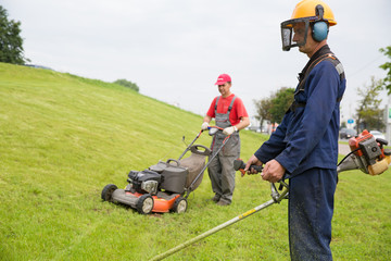 Gardeners mowing lawn with gas trimmer and lawnmower machine