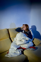 Naklejka premium young sick woman on couch wrapped in duvet feeling miserable