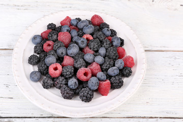 Iced berries on plate, on color wooden background