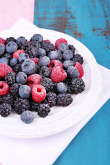 Iced berries on plate, on color wooden background