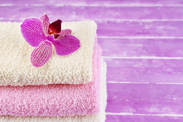 Orchid flower and towels on color wooden background
