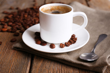 Cup of coffee and coffee beans on napkin on wooden background