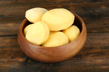 Raw peeled potatoes in bowl  on wooden background