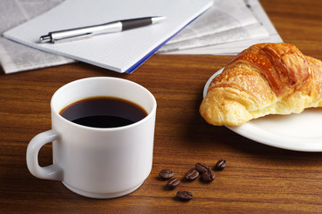 Coffee, croissant, newspaper and notepad