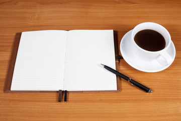 Open a blank white notebook, pen and cup of coffee on the desk