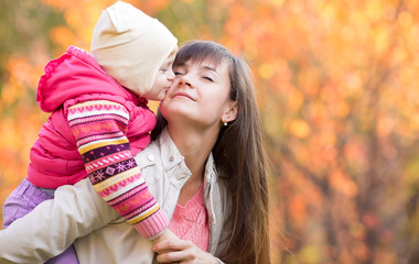 Beautiful woman with kid girl outdoors in fall. Child kissing mo