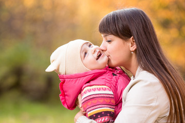 Young mother kissing kid girl outdoors in autumn park