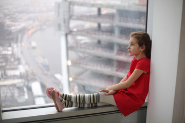 Little girl sitting on the windowsill of a large window