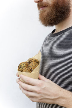 bearded guy holding falafel balls on takeaway paper cornet