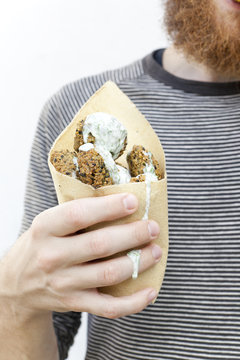 male hand holding falafel balls with dripping yogurt sauce