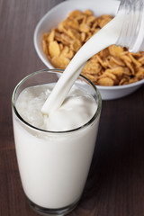 milk pouring into glass and bowl with cornflakes