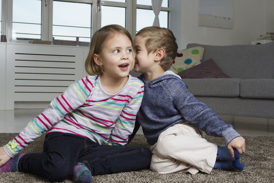 Brother and sister whispering on carpet in living room