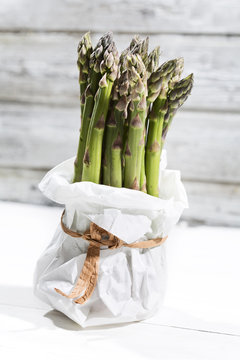 Bunch of green asparagus standing in white paper bag in front of white wood