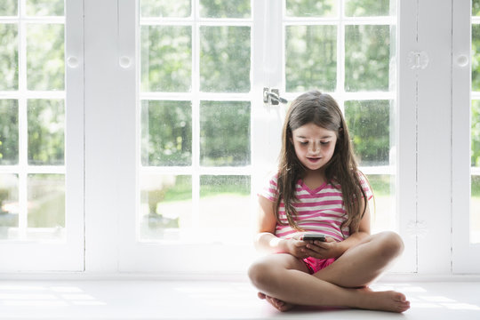 Girl with smart phone sitting at window