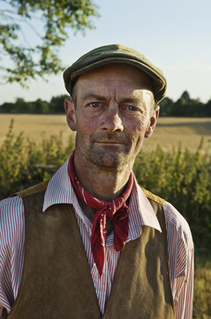 A man with a red neckerchief and flat hat, in working shirt and waistcoat. 