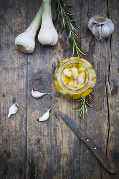 Fresh and pickled garlic cloves, garlic bulbs, rosemary and a knife on wooden table