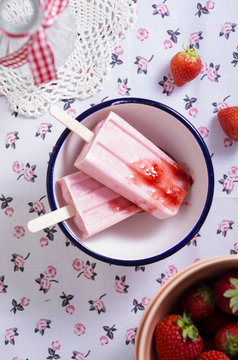 Bowl of two strawberry ice lollies and strawberries on cloth, elevated view