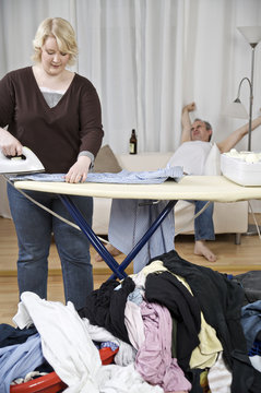 Woman ironing shirt with man in background leaning back