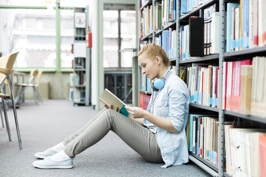 Student In A University Library Sitting On Floor Reading Book