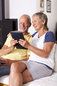 Senior couple sitting on couch using digital tablet