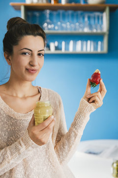 Portrait of young pregnant woman eating strawberry with mustard in her kitchen