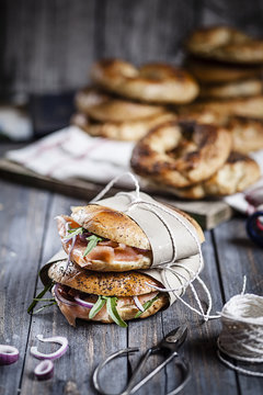 Two garnished home-baked bagels wrapped in paper, string and scissors on wood