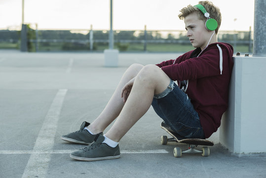 Serious teenage boy outdoors on skateboard listening to music