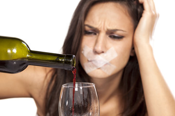 girl with sticky tape over her mouth pours wine into a glass