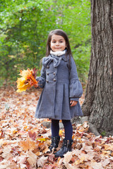 Little pretty girl with autumn leaves in an autumn park