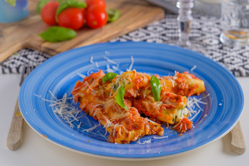 cannelloni pasta dish with tomatoe sauce on a blue plate with to