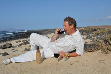The man is drinking red wine on the beach